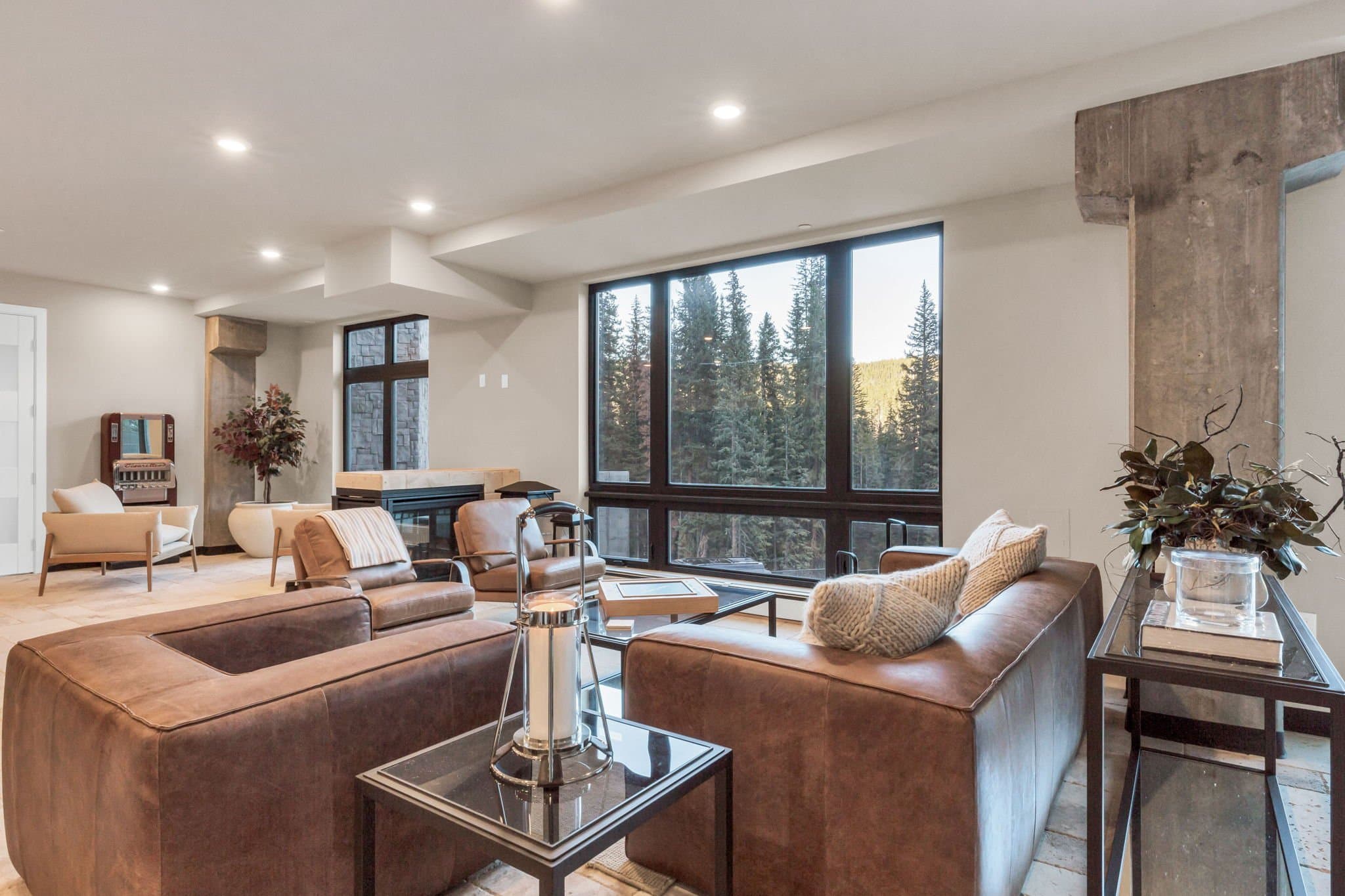 The club lounge at dusk, leather seating facing floor-to-ceiling windows onto snow-covered pines