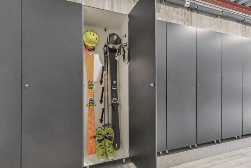 A row of grey ski lockers, one open showing skis, poles and a helmet