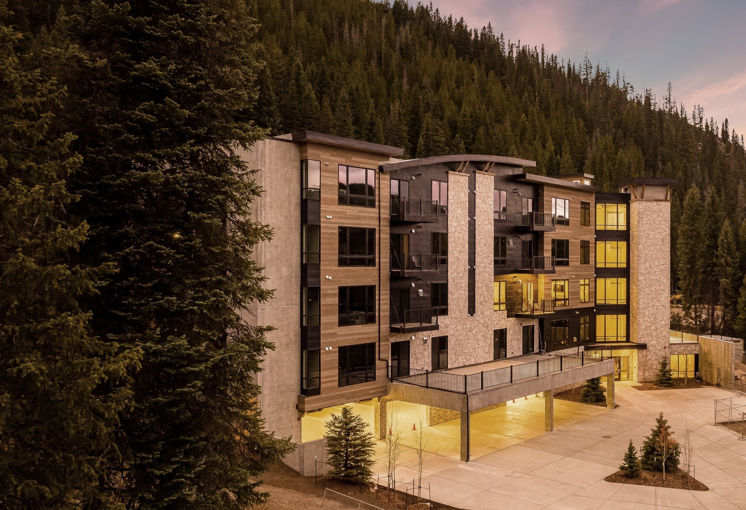 The U9200 building at dusk, lit windows against dark pines and mountain